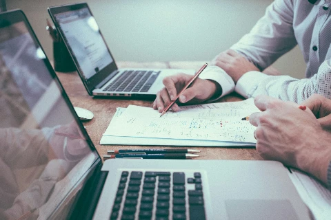 Zwei Personen arbeiten mit Laptops und Notizen an einem Schreibtisch